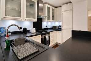 A modern kitchen with white cabinetry, stainless steel appliances, and a black countertop.