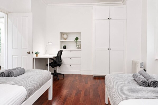 A bedroom with two beds, a desk, a chair, and a wardrobe.