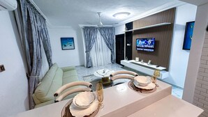 Een woonkamer met een bank, een eettafel met borden en glazen, een televisie aan de muur en een plafondventilator.
