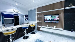 Een moderne keuken met een televisie, barstoelen en een klok.