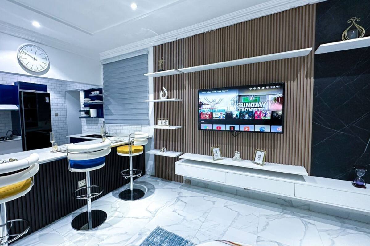 Een moderne keuken met een televisie, barstoelen en een klok.