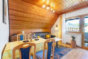 Um quarto acolhedor com teto de madeira, uma mesa de jantar com cadeiras, um sofá e uma janela com vista para edifícios.