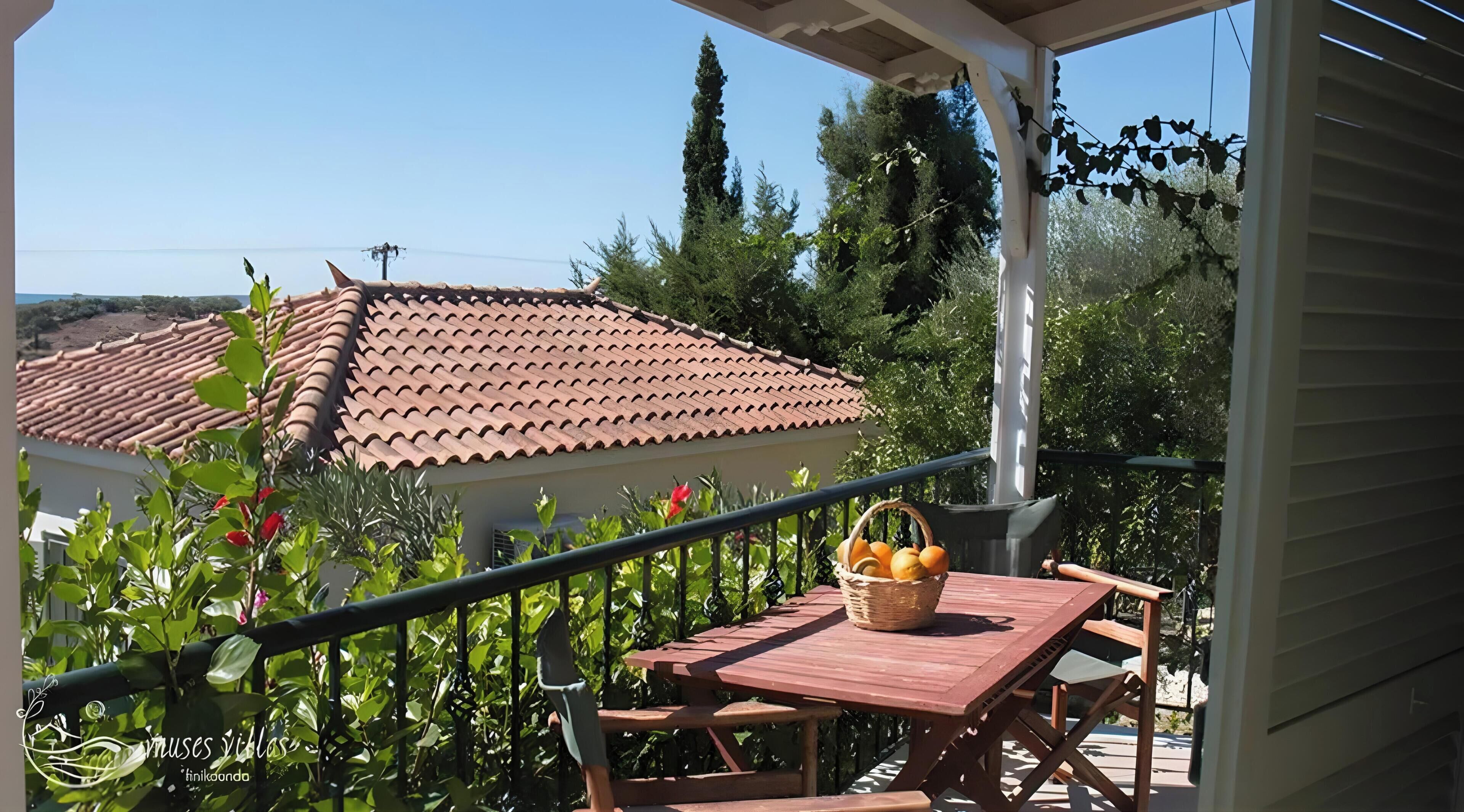 Una mesa de madera con una cesta en un balcón que ofrece vistas a una casa con tejado de tejas.