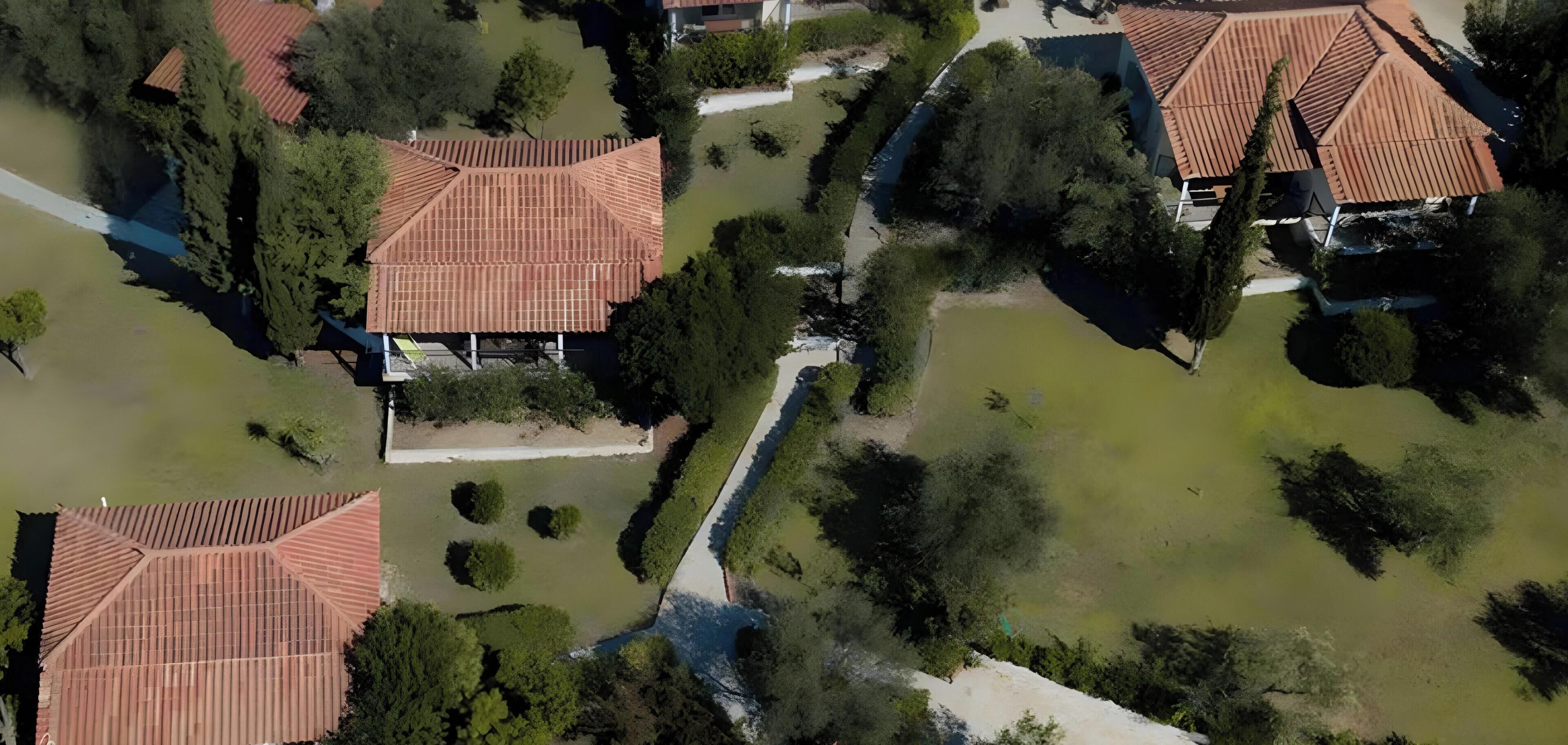 Vista aérea de una zona residencial con varias casas, un camino central y abundante vegetación.