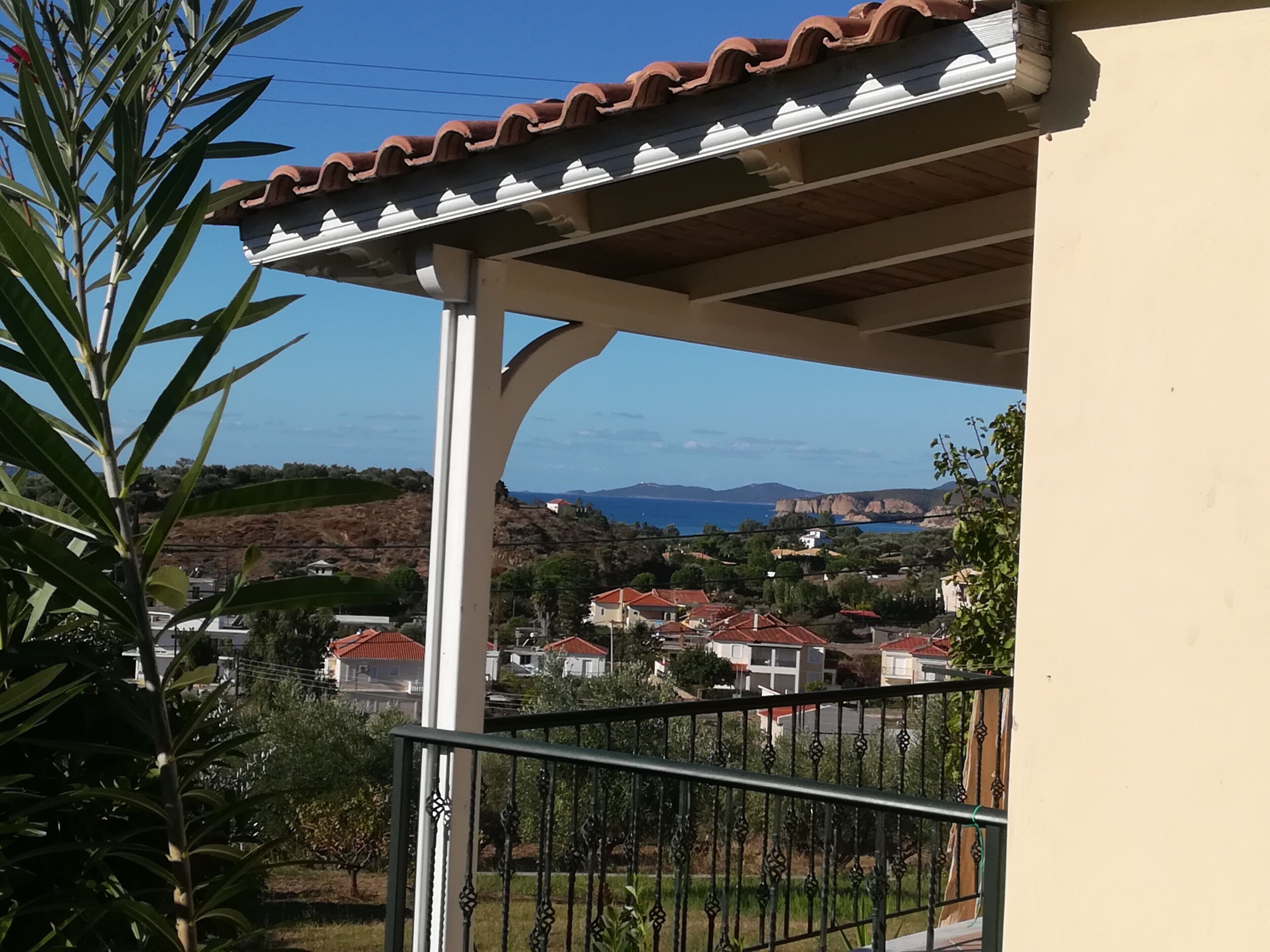 Un balcon donnant sur une ville côtière, avec une balustrade blanche et un toit recouvert de tuiles.