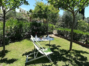 Um jardim ao ar livre com uma mesa posta para um evento, rodeado por vegetação exuberante e árvores.