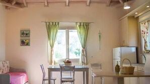 A cozy room with a bed, a table with chairs, a television, a window with curtains, and a kitchen area with cabinets and a refrigerator. - Country House 'No 3 Holiday Home' with Sea View, Wi-Fi, and Air Conditioning (Methoni)