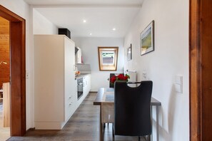 A narrow kitchen with white cabinets, a black chair at a table, and a window with a view of the outdoors. - Apartment 'Enzian' with Mountain View, Shared Garden and Wi-Fi (Bernau im Schwarzwald)