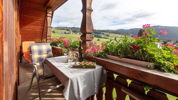 A wooden balcony with a table, chairs, and a chessboard.