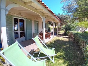 A covered patio with outdoor furniture, a door with shutters, and a garden area.