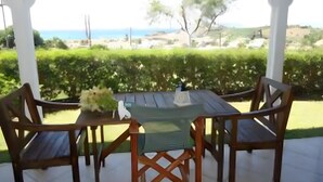 Eine Terrasse im Freien mit Tisch und Stühlen, Blick auf das Meer und ein gepflegter Garten.