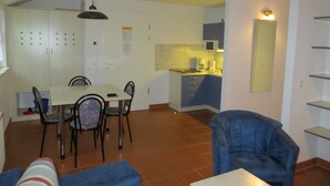 Un comedor con mesa y sillas, una cocina con armarios y electrodomésticos, y un sillón azul.