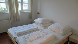 Una habitación con dos camas individuales, una ventana con cortinas, un radiador y una mesita de noche pequeña.