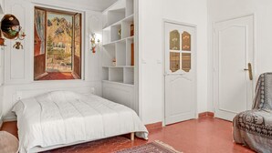 A bedroom with a bed, a built-in bookshelf, a door with a decorative panel, and a window with a painting. - Apartment '1st Floor' with Wi-Fi (Castellane)