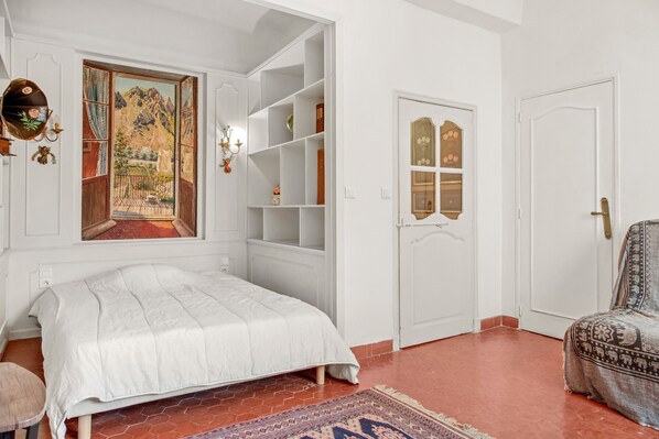 A bedroom with a bed, a built-in bookshelf, a door with a decorative panel, and a window with a painting.