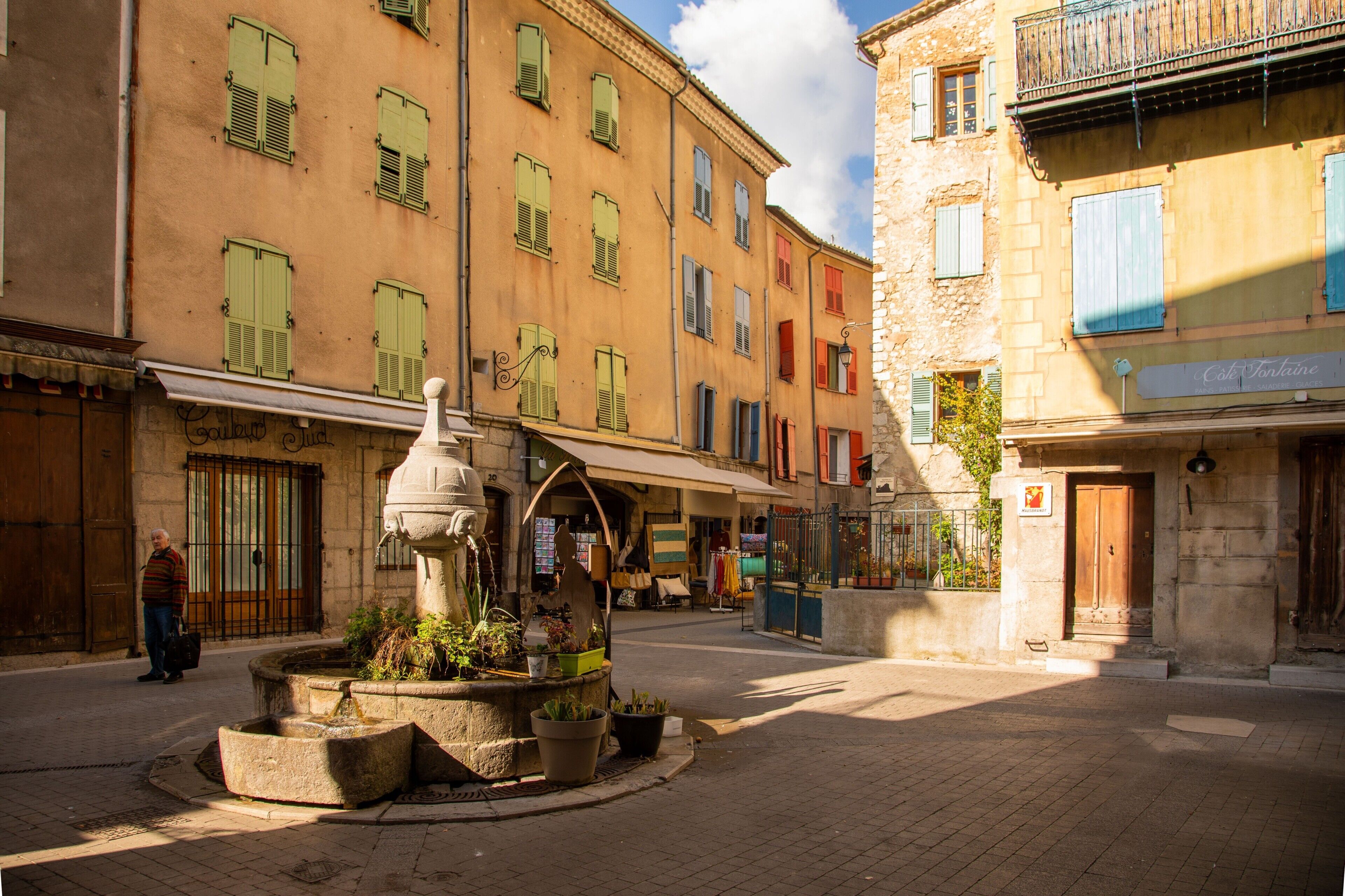 A street with buildings, a fountain, and a man walking.