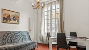 A room with a sofa, dining table, chairs, a chandelier, a painting, and a window with curtains. - Apartment '1st Floor' with Wi-Fi (Castellane)
