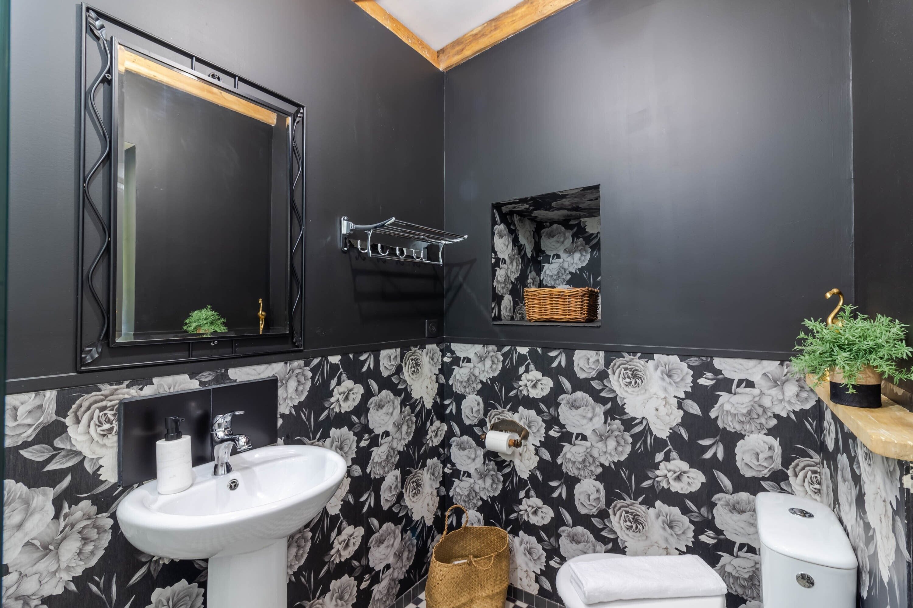 A bathroom with a sink, mirror, toilet, and a small shelf with a plant.