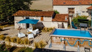 Un edificio de piedra con techo de tejas, piscina y mobiliario exterior.