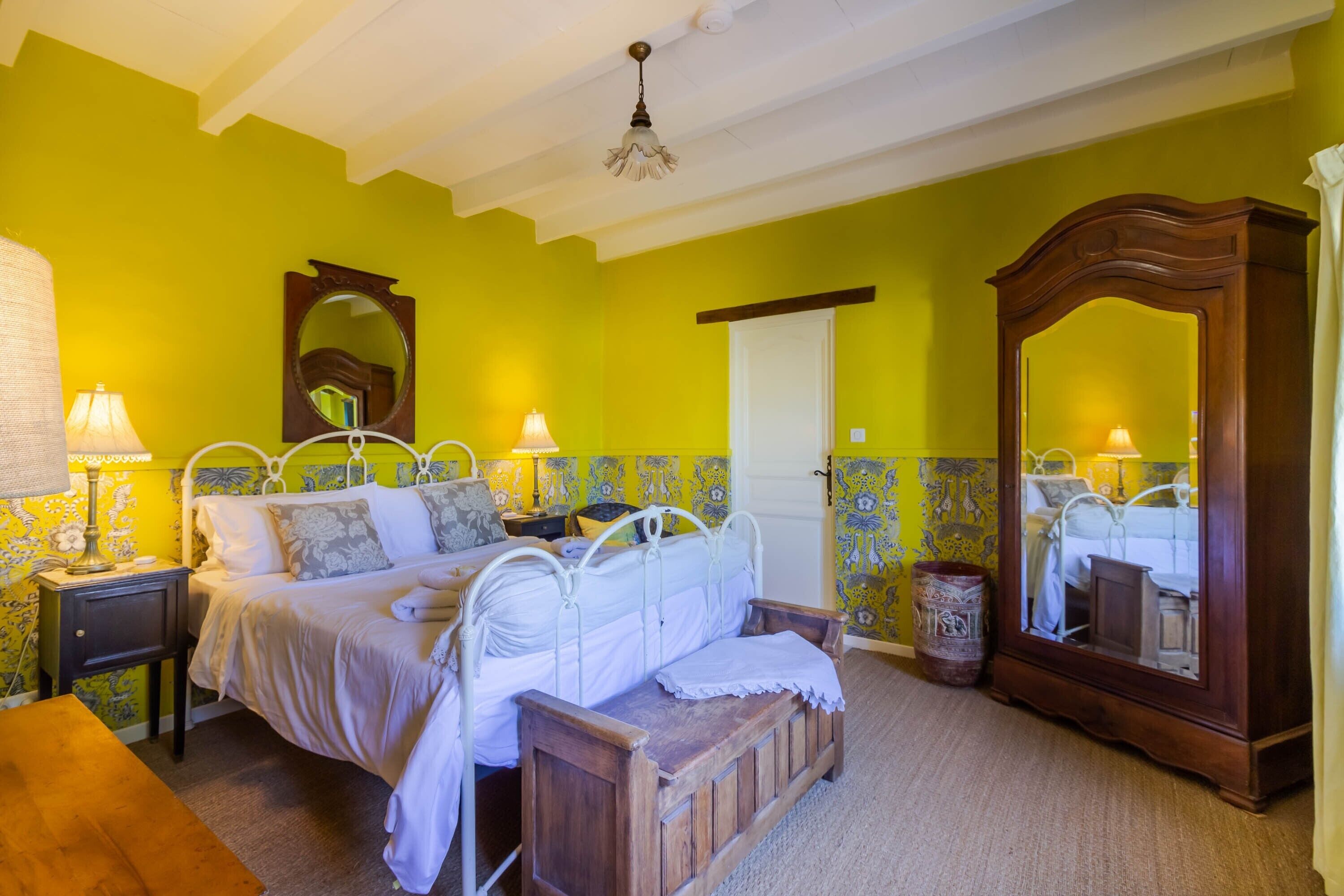 A room with a bed, bedside tables, a wooden bench, a mirror, and a door.