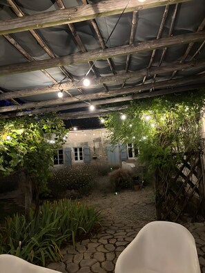 A covered outdoor area with a rustic wooden ceiling, stone paving, and a white chair.
