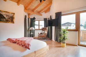 Un dormitorio con cama, una silla, televisor, ventana y una planta.