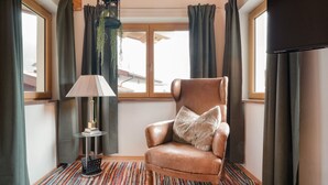 Una habitación con un sillón de cuero, una lámpara, una alfombra estampada y vistas a través de una ventana.