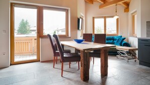 Un comedor con una mesa de madera, sillas y un tazón azul. Hay un sofá y un televisor al fondo.
