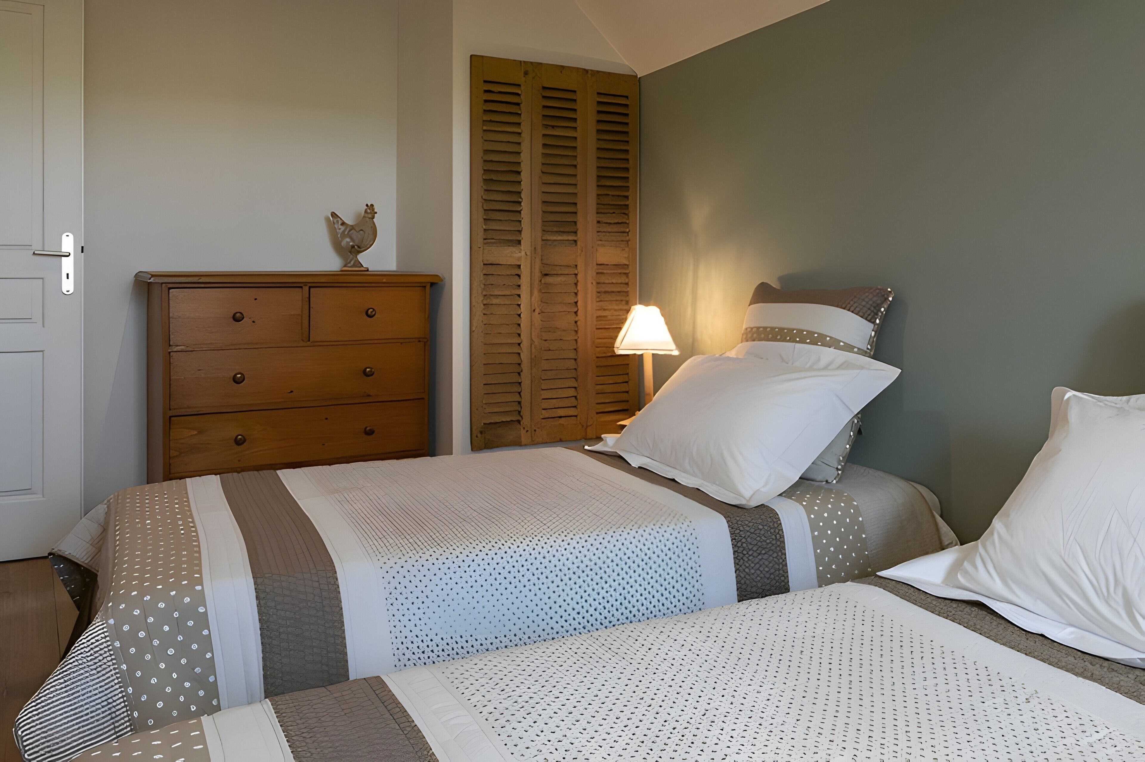 A bedroom with two beds, a wooden dresser, a lamp, and a closet with shutters.