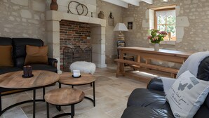 A cozy living room with a fireplace, leather sofa, wooden coffee table, and a window with a view. - La Clef des Champs - Pool and Jacuzzi - Lémeré (Lémeré)