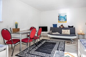 Ein Wohnzimmer mit einer Couch, roten Sesseln, einem Fernseher und einem Esstisch mit Stühlen.
