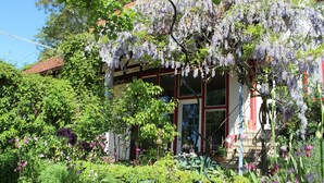 Un jardín con diversas plantas y flores, una casa de techo rojo y un regadera verde.