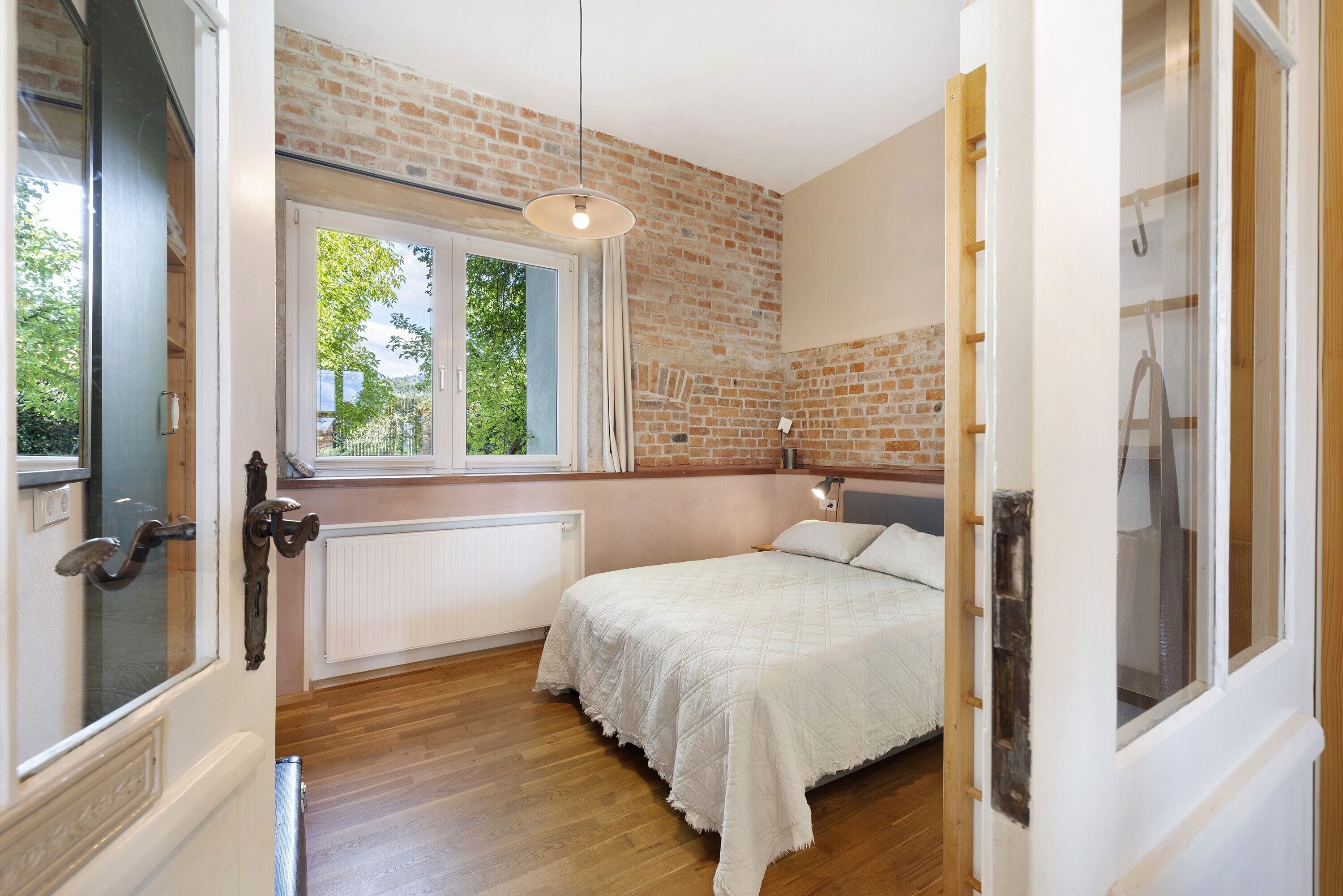 A bedroom with a brick wall, a window, a bed, and a radiator.