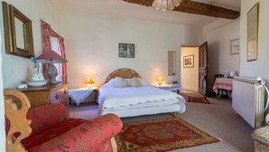 A bedroom with a bed, bedside tables, a wooden chair, a red sofa, a patterned rug, and a ceiling light. - Queen’s Room with Pool and Garden (Sauzet)