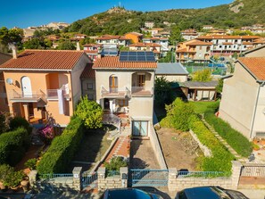 A residential area with houses featuring balconies, solar panels, and a hillside in the background.
