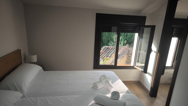 A hotel room with two beds, a window with a view of a garden and buildings, and a nightstand with a lamp. - Ideal for Families (Alájar)