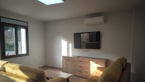 A modern living room with a sofa, a TV mounted on the wall, and a window with a view of greenery. - Ideal for Families (Alájar)