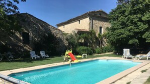 A swimming pool with a slide, surrounded by lounge chairs and a stone building.