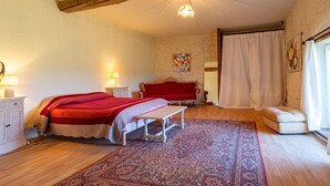 A bedroom with a bed, bedside tables, a bench, a red sofa, a rug, and a window with curtains.