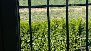 A view through a window with a metal grid, displaying a green field and distant hills.