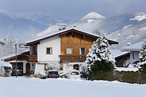 Een houten huis met twee verdiepingen en een garage, omgeven door besneeuwde bergen.