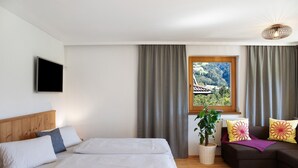 A bedroom with a bed, a sofa, a TV, a window with curtains, and a plant. - Apartment 'Mia' with Mountain View, Balcony and Wi-Fi (Ried im Zillertal)