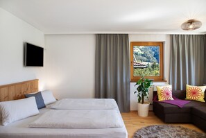 A bedroom with a bed, a sofa, a TV, a window with curtains, and a plant. - Apartment 'Mia' with Mountain View, Balcony and Wi-Fi (Ried im Zillertal)