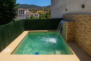 Une piscine rectangulaire agrémentée d’une cascade, entourée d’une haie et d’un mur en briques.