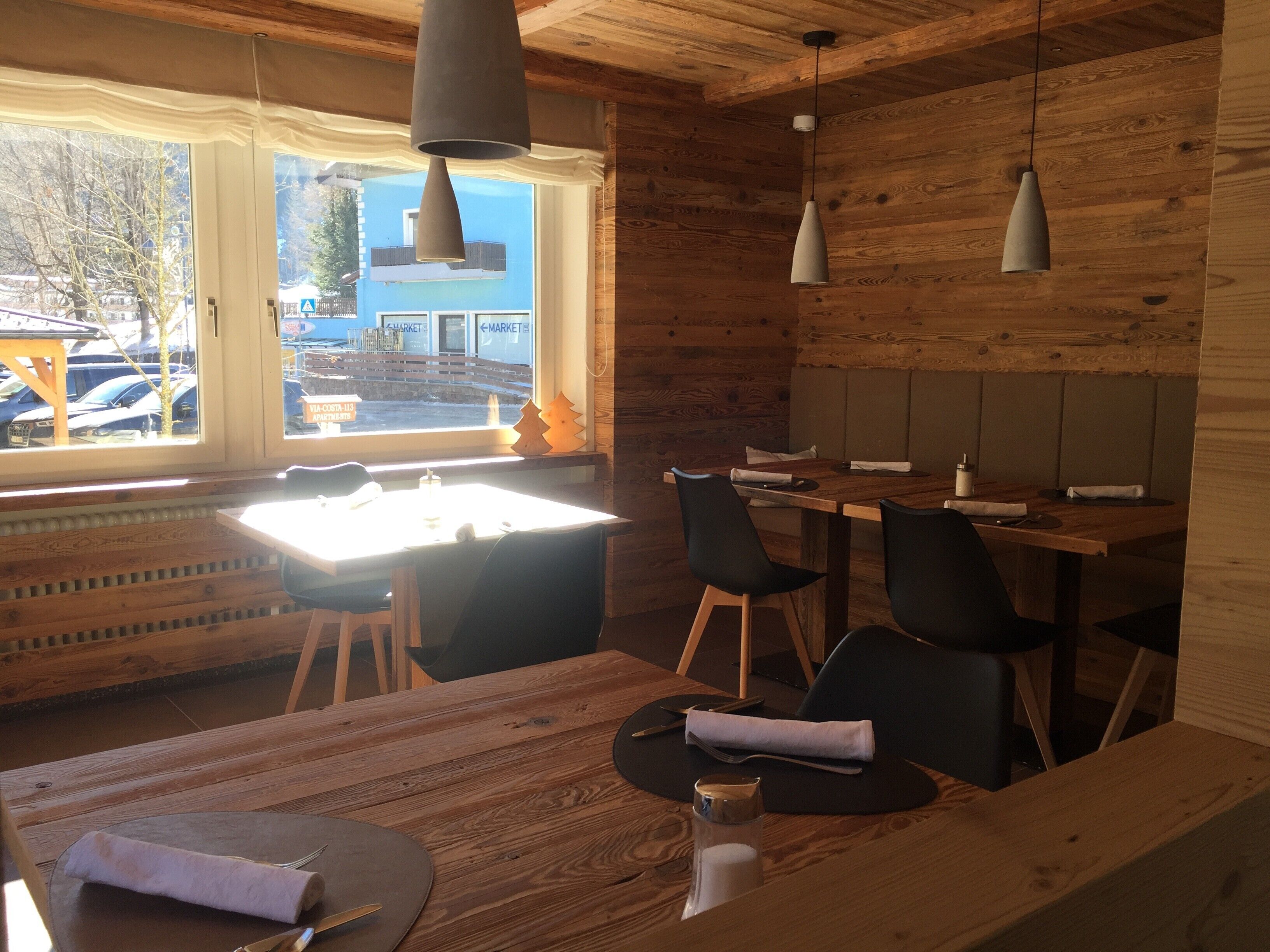 A wooden interior with a dining area, tables, chairs, pendant lights, and a view of the outside.