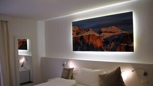 Ein Hotelzimmer mit einem Bett, einem Nachttisch, einer Wandlampe und einem Bild von Bergen.