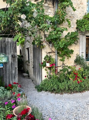Une cour rustique avec un mur en pierre, une porte en bois et des plantes en pot.