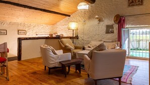 Une pièce rustique avec des poutres en bois, des murs en pierre, un canapé, des fauteuils, une petite table et une lampe.