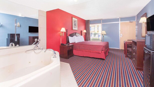 A hotel room with a large bathtub, a red accent wall, a bed with white bedding, and a television. - Hotel Inn Albany (Albany)