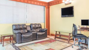A living room with a leather sofa, a glass coffee table, a desk with a computer, and a TV mounted on the wall. - Hotel Inn Albany (Albany)